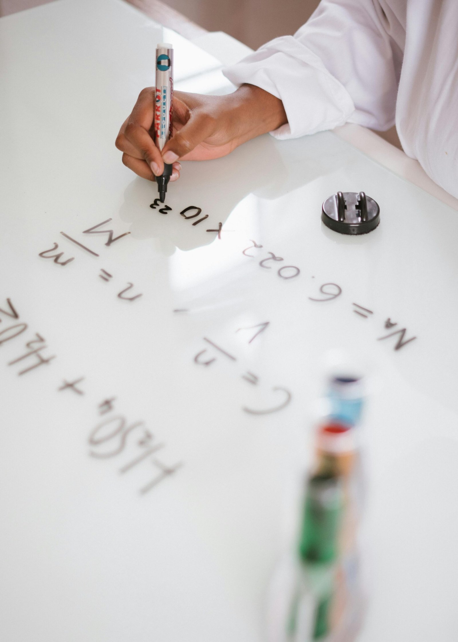 Unrecognizable ethic chemist in uniform writing with marker formulas on whiteboard after analysis chemical reaction on test tubes in laboratory
